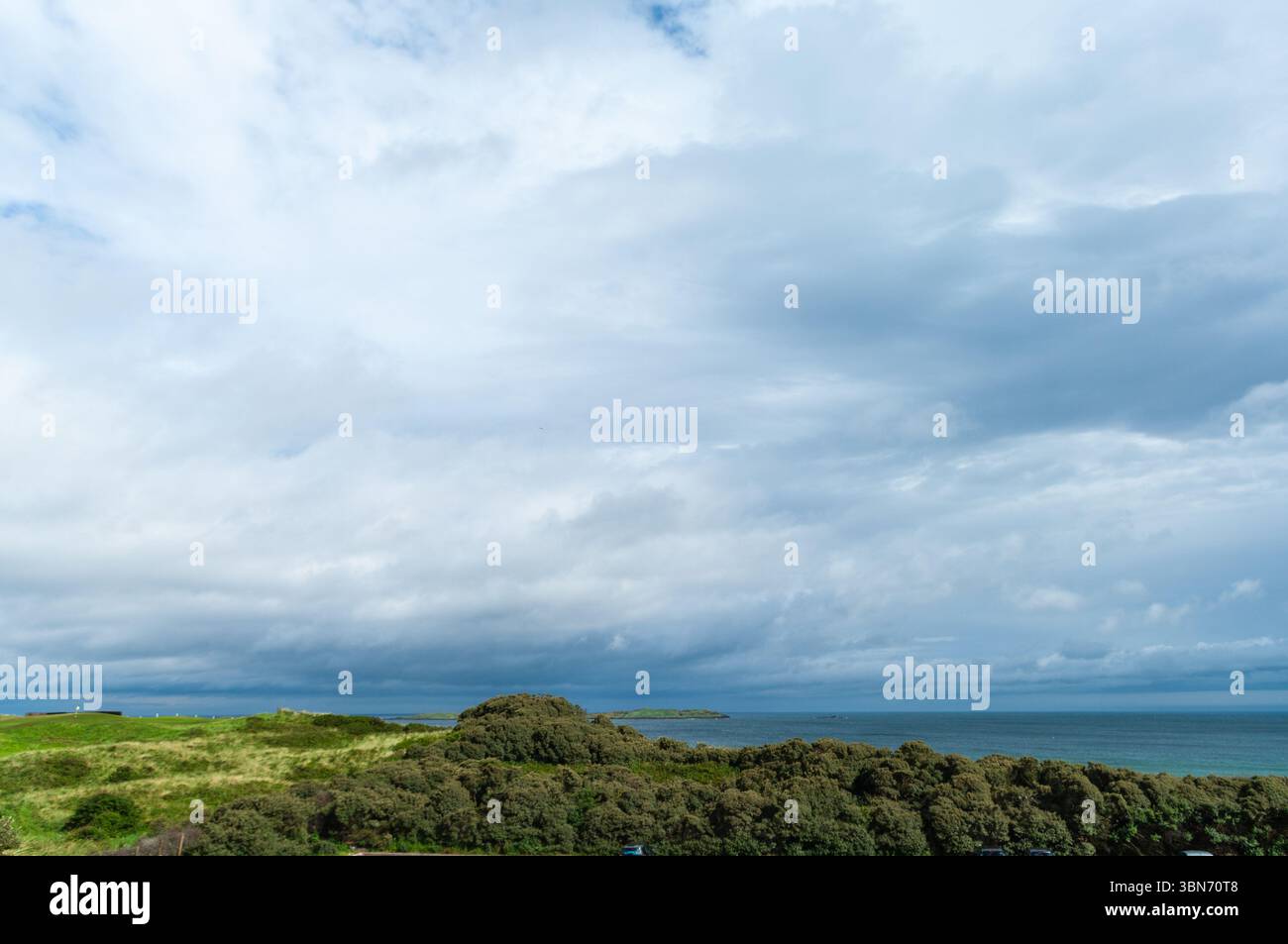 Un ciel nuageux avec une colline en arrière-plan. Le ciel est principalement nuageux avec quelques taches de bleu Banque D'Images