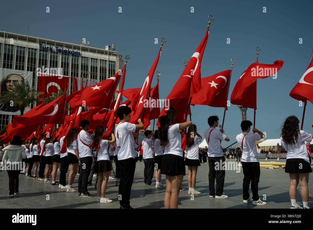 Izmir, Turquie - 19 mai 2025 : des adolescents se tiennent en formation avec des drapeaux turcs pendant les célébrations de la Journée de la Jeunesse, avec un grand portrait d'Ataturk sur le bâtiment BE Banque D'Images