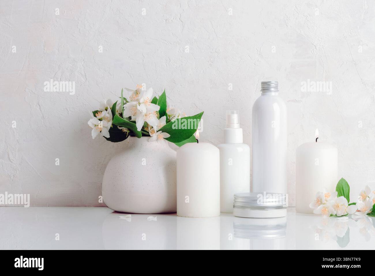 Bouteilles cosmétiques blanches et bougies avec des fleurs de jasmin sur fond blanc. Spa et concept de bien-être. Vue de face. Banque D'Images