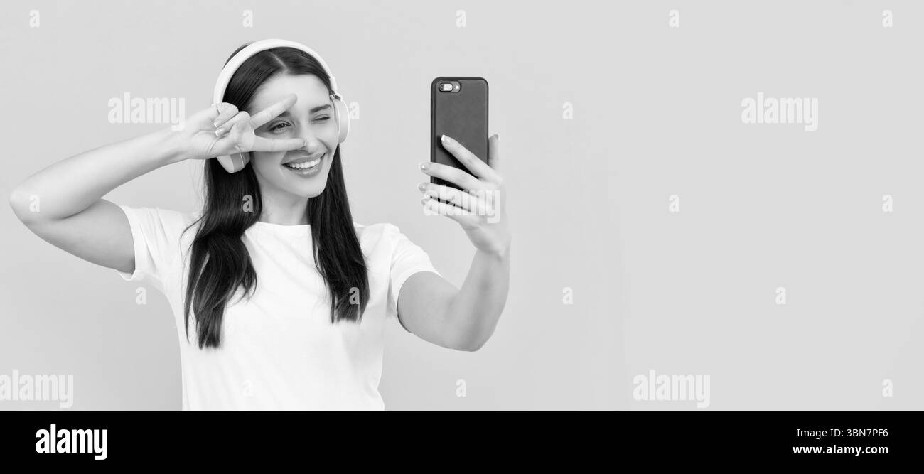 femme positive en chemise blanche dans le casque faisant selfie sur le téléphone avec le geste de paix, selfie. Femme isolée visage portrait, bannière avec espace de copie. Banque D'Images