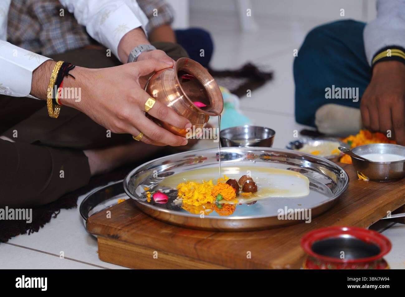 Un rituel hindou traditionnel (puja) est exécuté. On voit une personne verser de l'eau ou un liquide sacré d'un kalash en cuivre (pot) dans un thali Banque D'Images