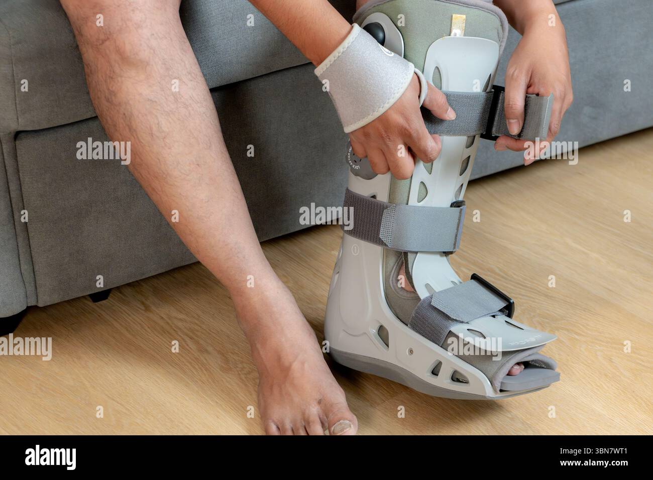 Homme asiatique assis sur le canapé appliquant une attelle de jambe, symbolisant la récupération à la maison et la valeur de l'assurance accident. Banque D'Images