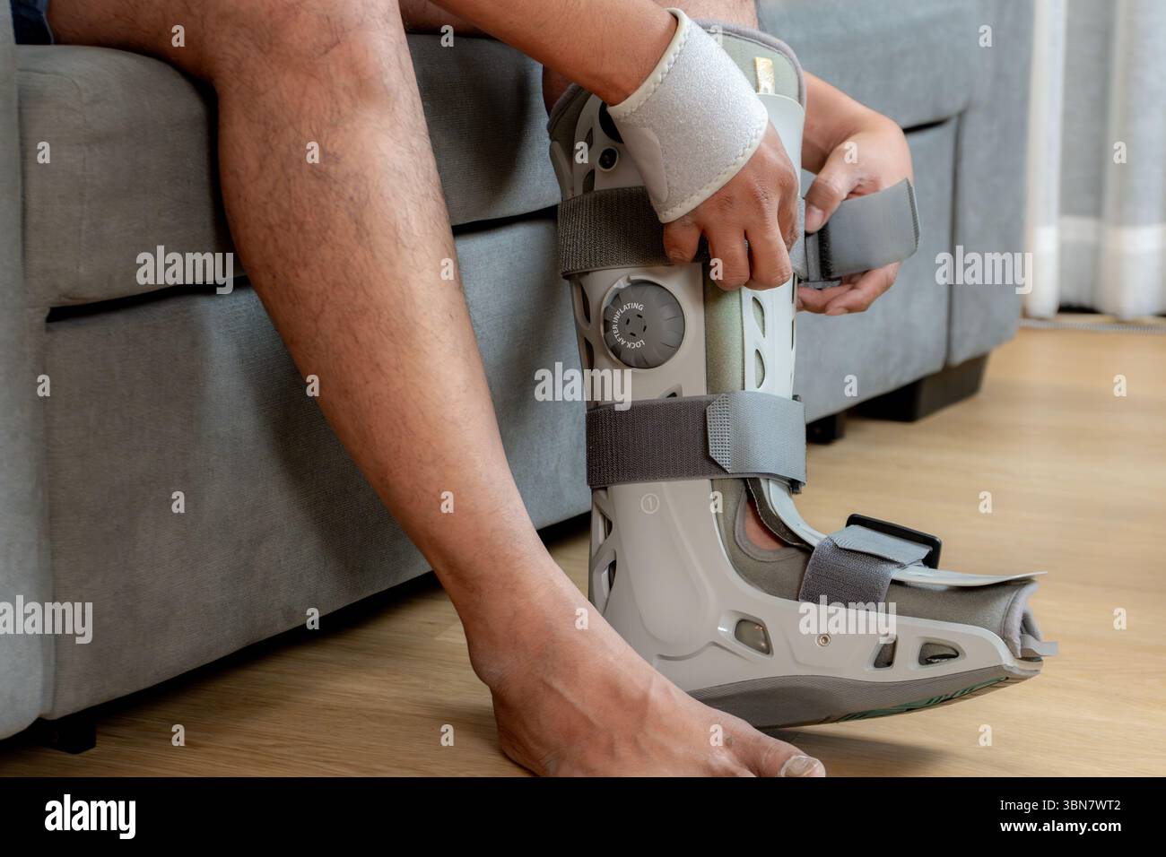 Homme asiatique assis sur le canapé appliquant une attelle de jambe, symbolisant la récupération à la maison et la valeur de l'assurance accident. Banque D'Images
