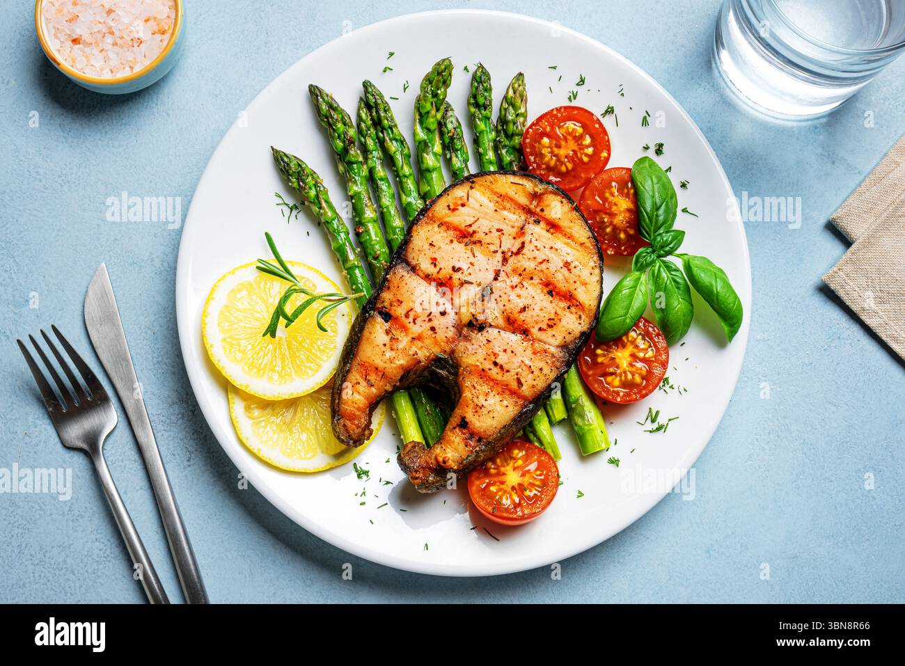 Steak de saumon grillé avec asperges vertes, tomates et tranches de citron sur fond bleu, vue de dessus. Repas équilibré et sain, déjeuner céto. Banque D'Images