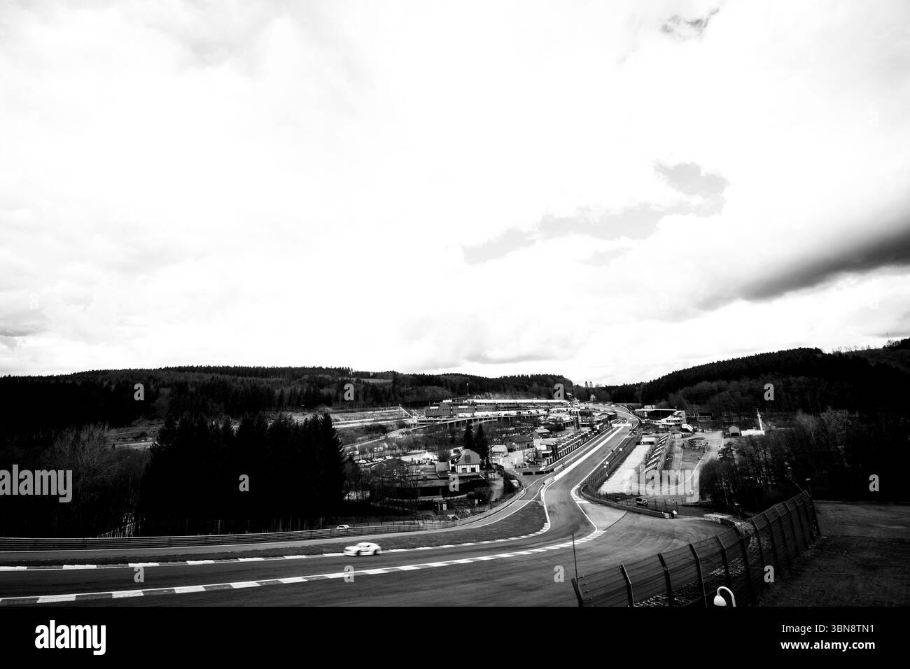 Capture dynamique en noir et blanc du circuit de course de Spa-Francorchamps avec une voiture qui roule à grande vitesse, des virages spectaculaires et un ciel spectaculaire. Banque D'Images