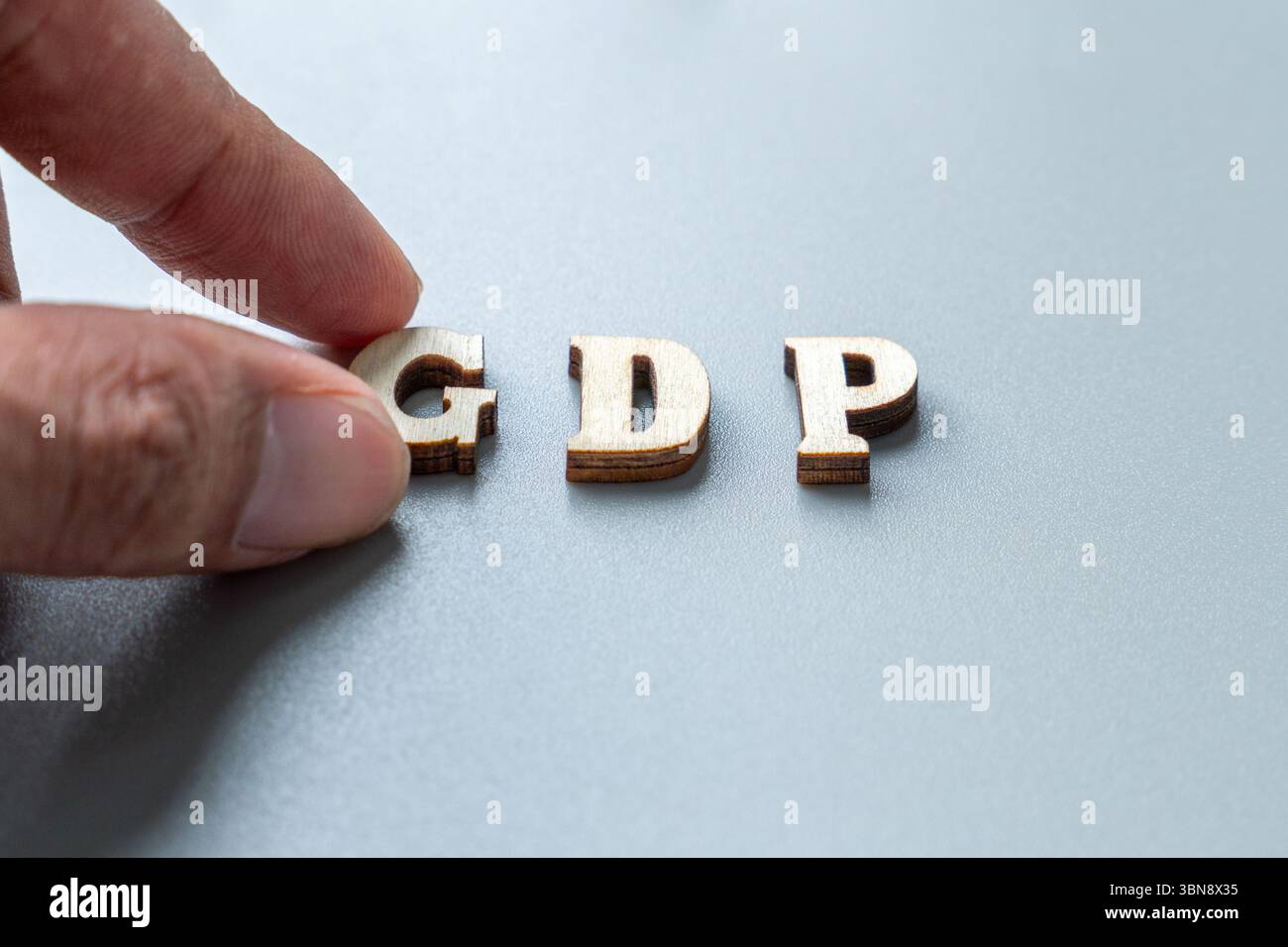 Un doigt ajustant des lettres d'imprimerie en bois qui épellent « GDP ». Produit intérieur brut, mesure économique, croissance, analyse de données, économie nationale Banque D'Images