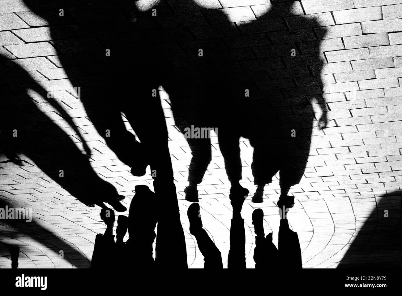 Silhouette d'ombre d'un groupe de personnes marchant sur le trottoir pavé, en noir et blanc contraste élevé Banque D'Images