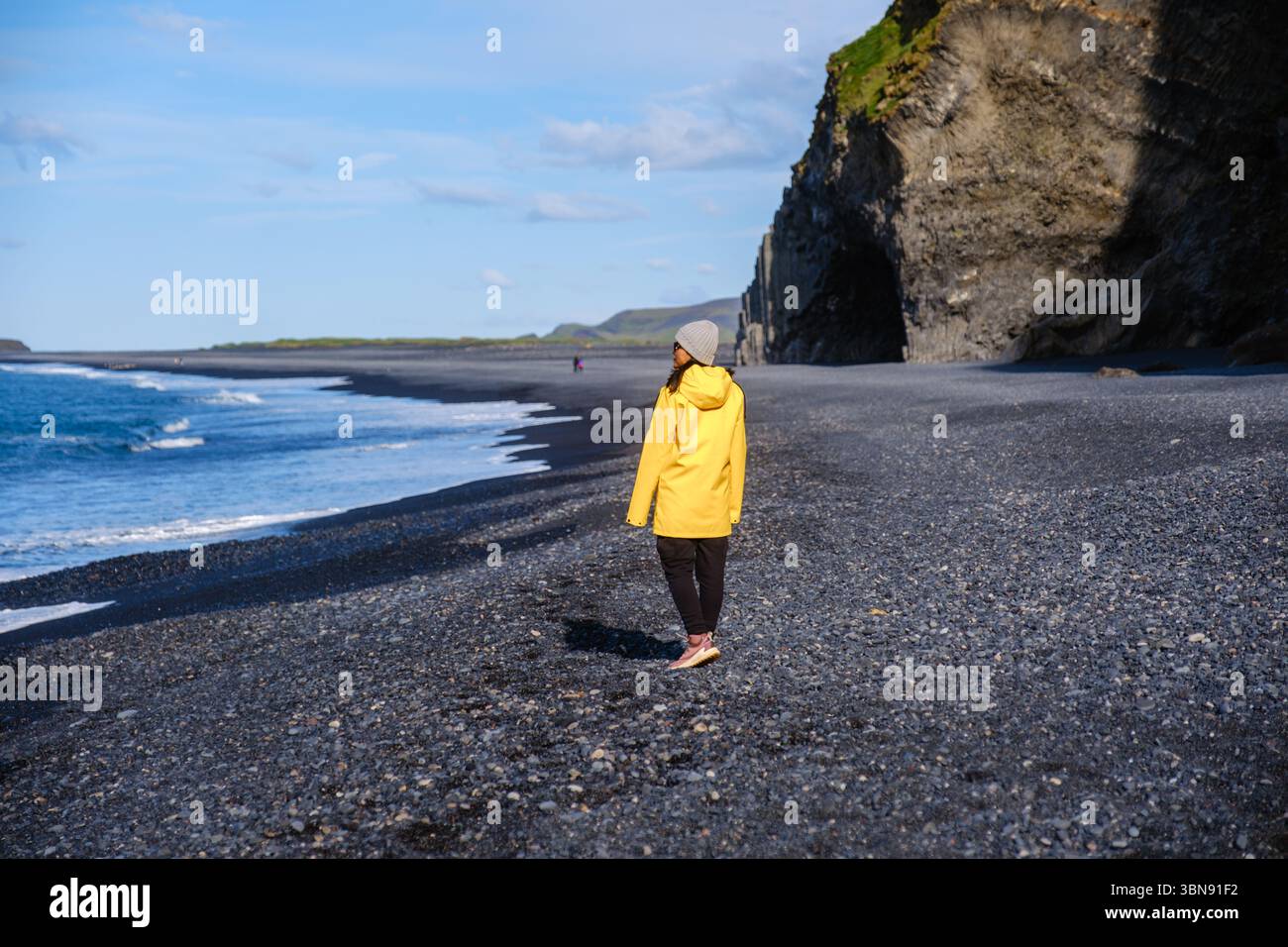 Un voyageur vêtu d'une veste de pluie jaune vif se promène le long du sable noir unique de Reynisfjara Beach Iceland Banque D'Images