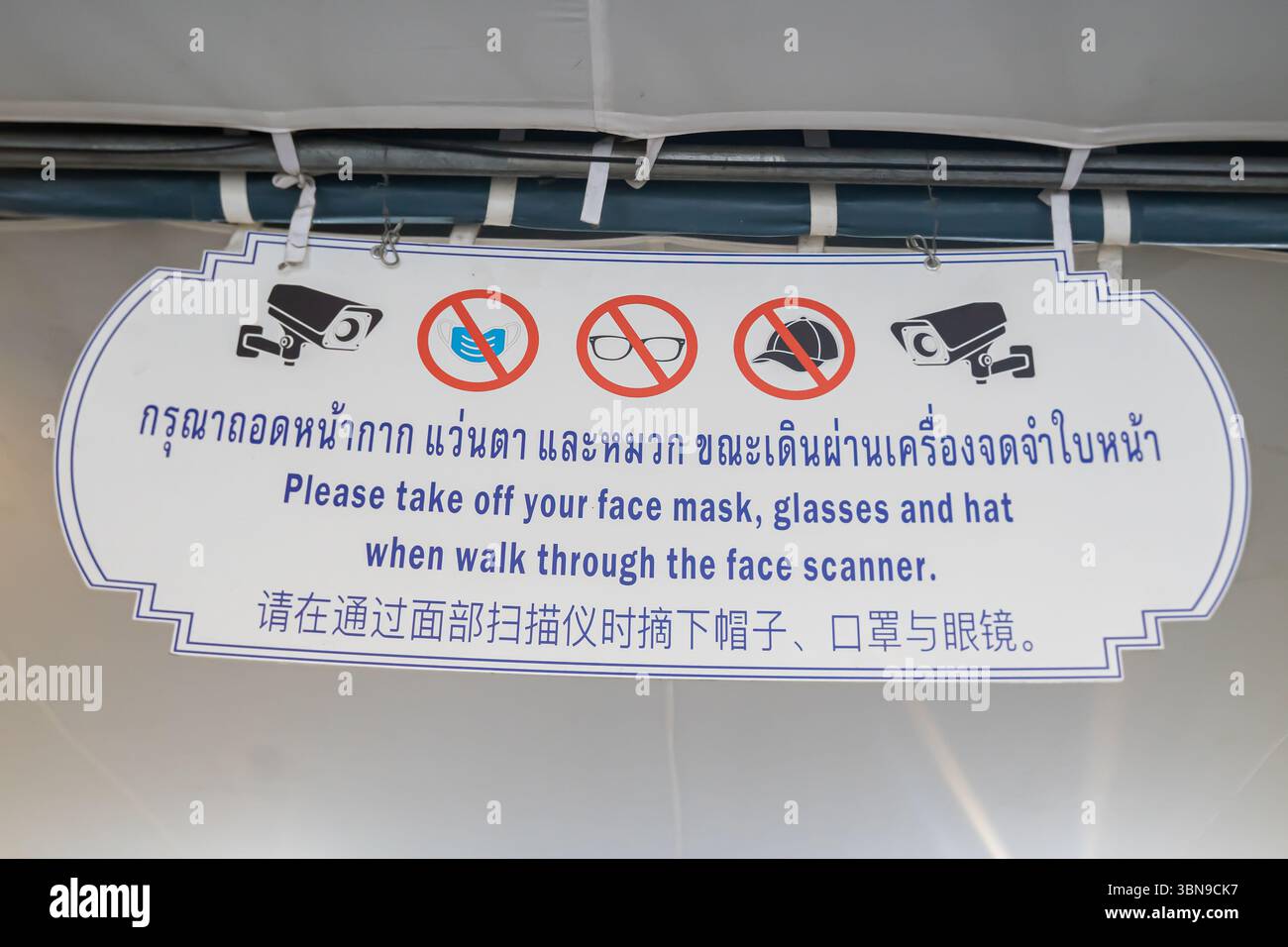 Un panneau indique aux gens d'enlever les masques faciaux, les lunettes et les chapeaux avant de marcher à travers un scanner de visage, en trois langues, Musée national de Bangkok Banque D'Images