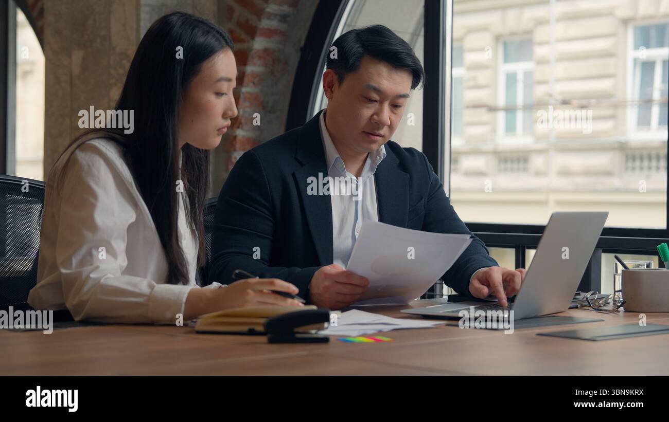 Deux directeurs d'entreprise collègues des collègues asiatiques travaillent ensemble des documents de travail d'équipe analysent la femme chinoise fille femme d'affaires japonaise homme coréen Banque D'Images