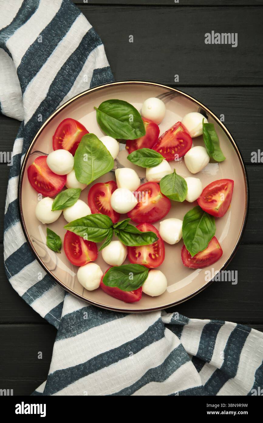 Salade Caprese italienne avec tomates cerises, mozzarella, basilic sur assiette sur fond noir. Vue de dessus Banque D'Images
