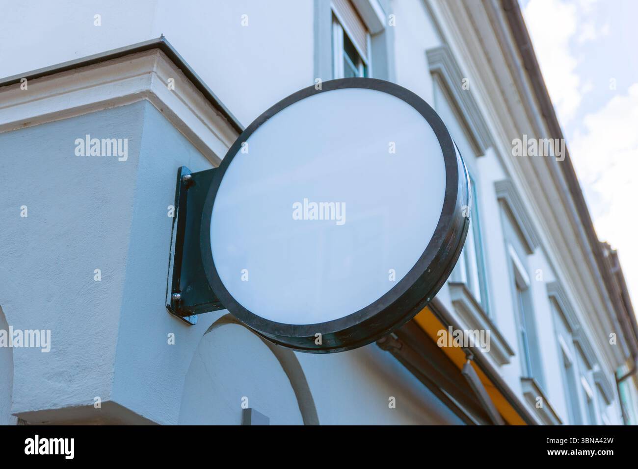 Signalisation blanche ronde montée sur la façade du bâtiment, idéale pour la marque, les maquettes d'entreprise ou les présentations de conception de vitrine commerciale dans les environnements urbains Banque D'Images