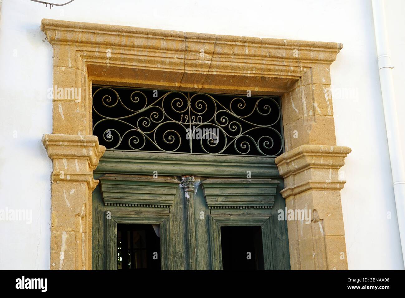 Nicosie (Lefkosia), Chypre, la dernière capitale divisée du monde, Un bâtiment blanc avec une porte en bois vert, qui est au centre de l’attention. La porte est ornée d'une grille décorative en métal avec un motif tourbillonnant et le numéro '1920' dessus. La porte est encadrée par une arche en pierre jaune, et l'extérieur du bâtiment est principalement blanc avec quelques accents de pierre beige clair ou crème. La porte a un élément décoratif sur le dessus, éventuellement une petite pièce décorative ou moulure. L'image est prise sous un angle légèrement bas, soulignant la hauteur de la porte et les détails architecturaux du Banque D'Images
