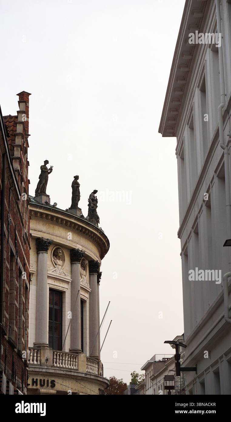 Anvers, deuxième plus grande ville belge, située sur l'Escaut en Belgique., Théâtre Bourla. Une scène de rue avec un bâtiment proéminent avec une façade incurvée et une série de statues sur son toit. Le bâtiment est principalement blanc avec une section de couleur crème ou beige à la base, et il a un style architectural classique avec des colonnes et un fronton. Les statues sur le toit sont de couleur sombre et semblent être des figures classiques. La rue est bordée de bâtiments de styles architecturaux variés, dont un bâtiment en briques sur la gauche et un bâtiment blanc sur la droite. Le ciel est couvert, Banque D'Images