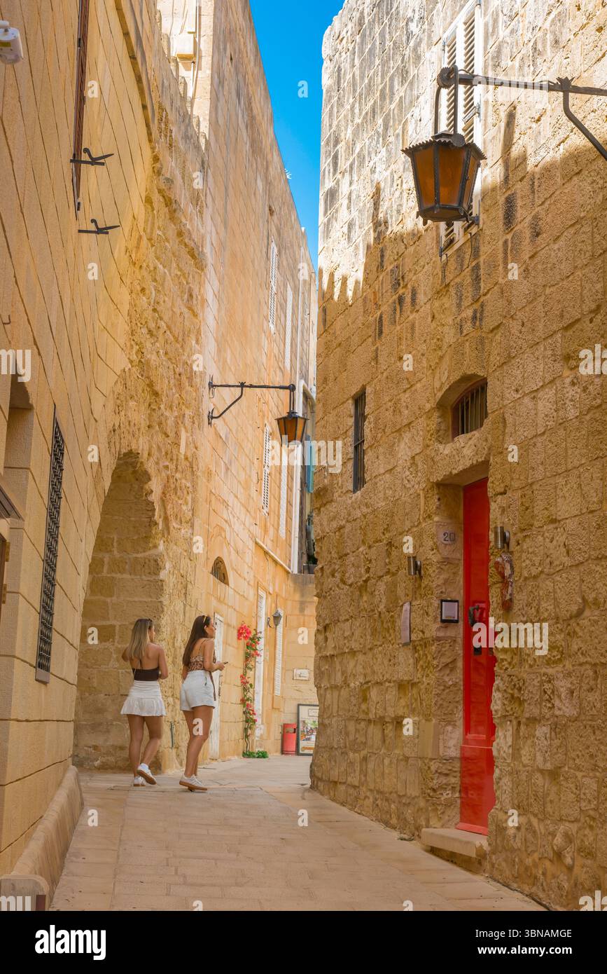 Mdina Malta Street, vue en été de deux jeunes femmes touristes explorant une rue sinueuse étroite dans la ville fortifiée historique de Mdina, Malte Banque D'Images