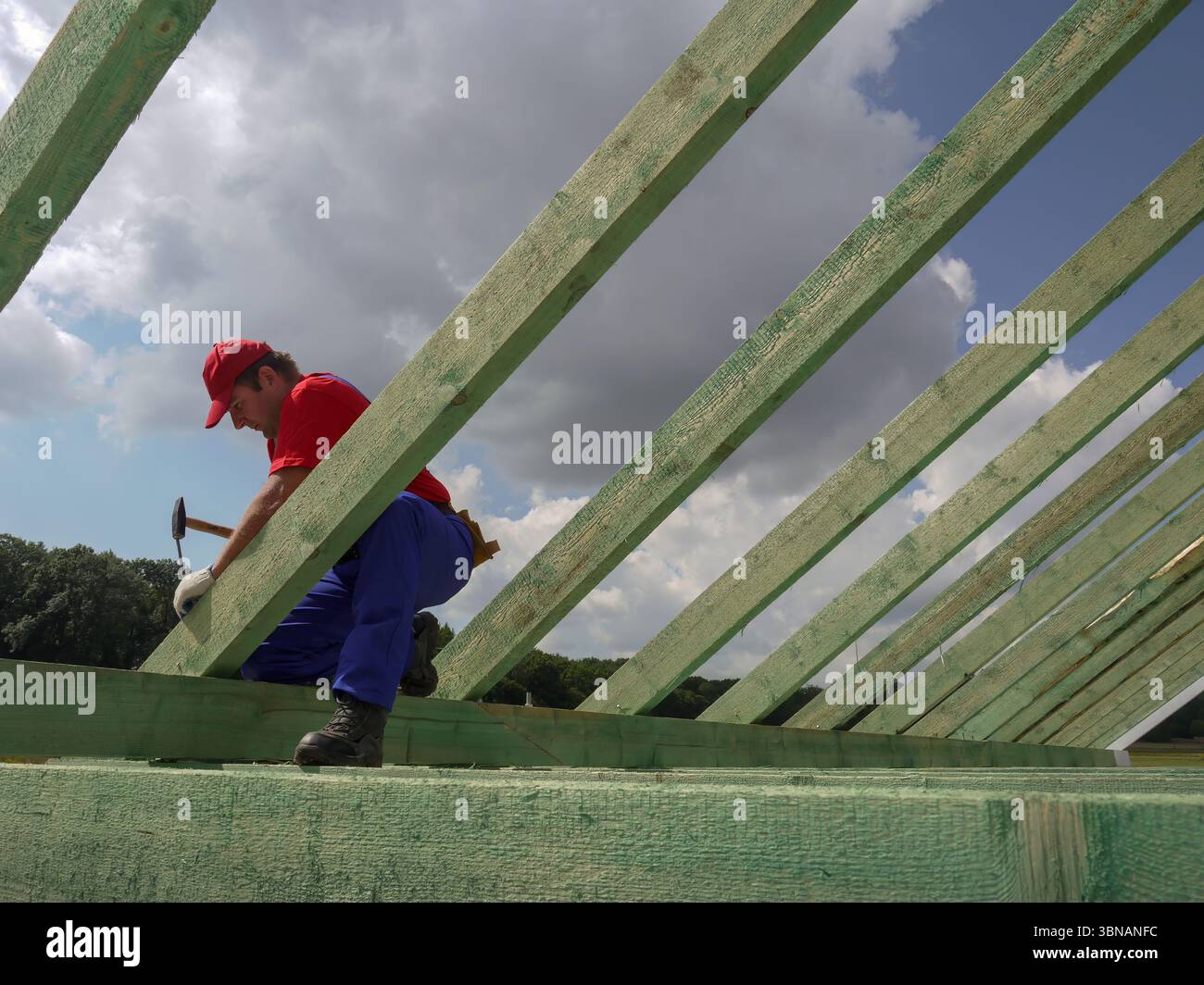 Travailleur de la construction dévoué s'engageant dans la menuiserie, attachant des fermes en bois sur une structure, sous un ciel ouvert Banque D'Images