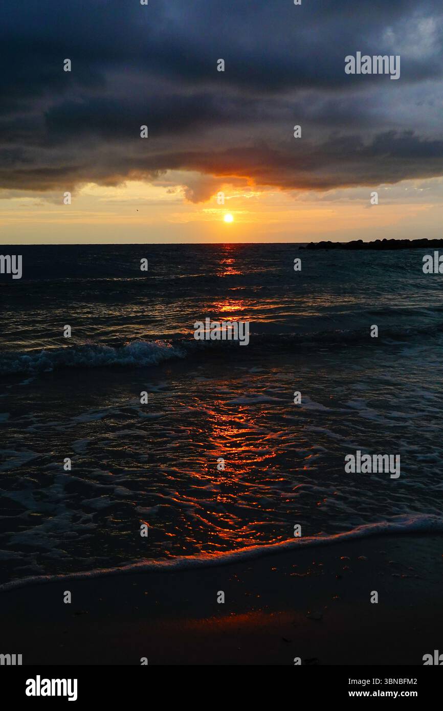 Alors que le soleil se couche, la lumière se reflète sur les vagues dans l'eau avec des nuages d'orage roulant au-dessus du ciel. Banque D'Images