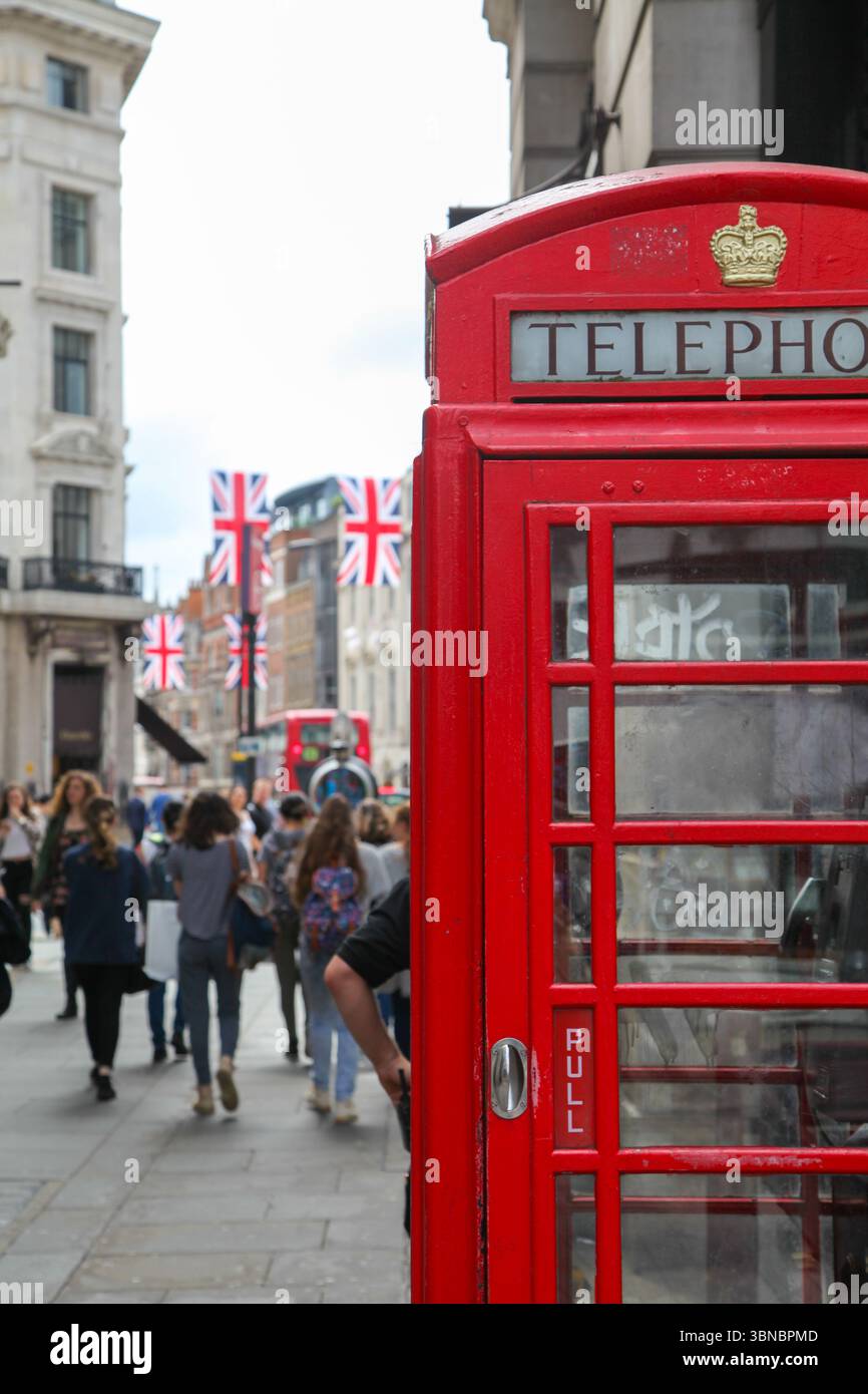 Cabine téléphonique rouge sur la rue animée de Londres avec des piétons, drapeaux anglais et zone commerçante en arrière-plan. Banque D'Images