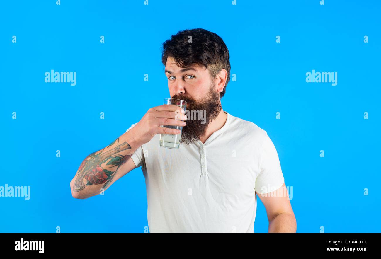 Bel homme barbu un verre d'eau douce. Homme attrayant en t-shirt blanc décontracté buvant de l'eau filtrée le matin. Mode de vie sain, bon Banque D'Images