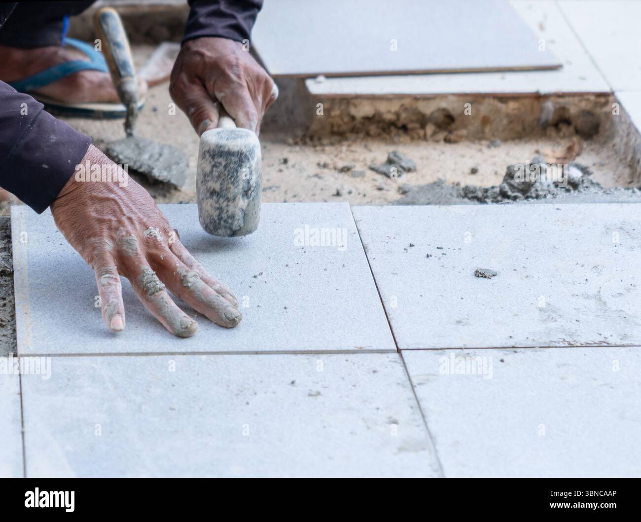 Le travailleur nivelle les carreaux de sol installés en les tapant avec un maillet en caoutchouc. Banque D'Images