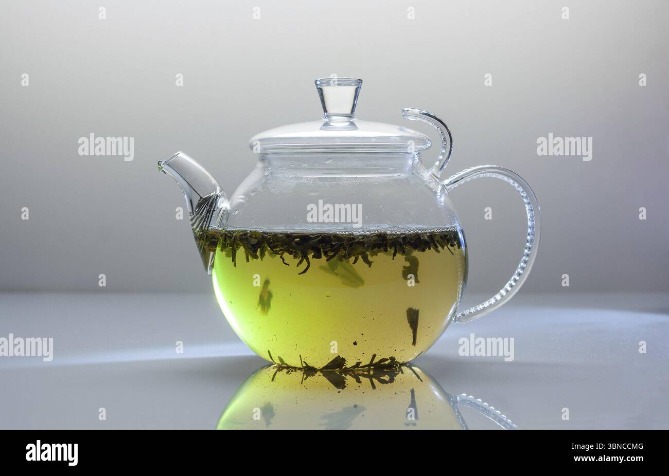 Une théière transparente avec une tisane jaune se tient sur une table en verre blanc Banque D'Images