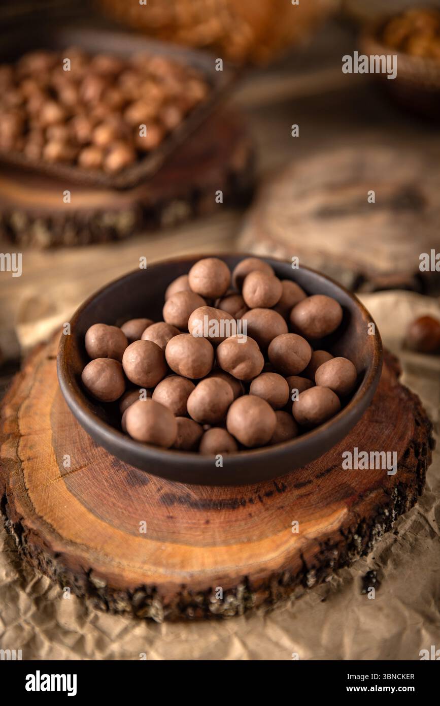 Les noisettes enrobées de chocolat sont présentées dans un bol, placé sur une surface en bois, créant une scène culinaire douce et rustique Banque D'Images