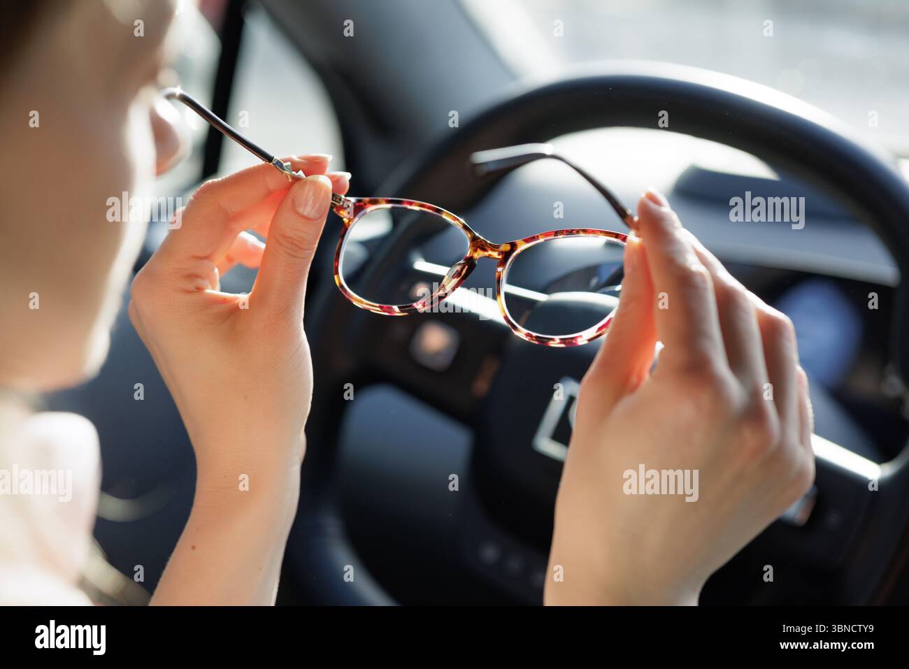 Gros plan d'une femme tenant des lunettes à l'intérieur de la voiture, lumière naturelle soulignant la clarté de la vision et la conduite en toute sécurité. Banque D'Images