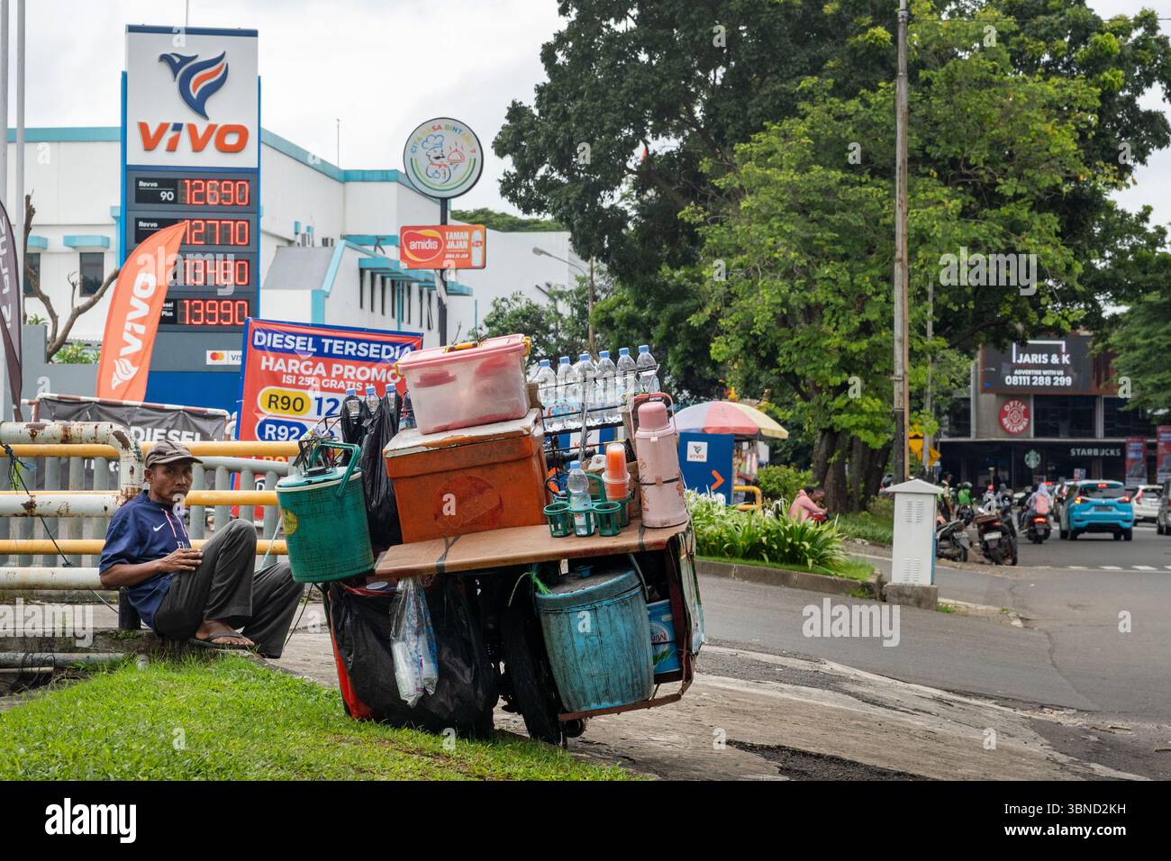 Jakarta, Indonésie - 30 janvier 2025 : un homme est assis sur le bord de la route avec un chariot plein de bouteilles d'eau. Le chariot est sur le côté et il porte un blu Banque D'Images