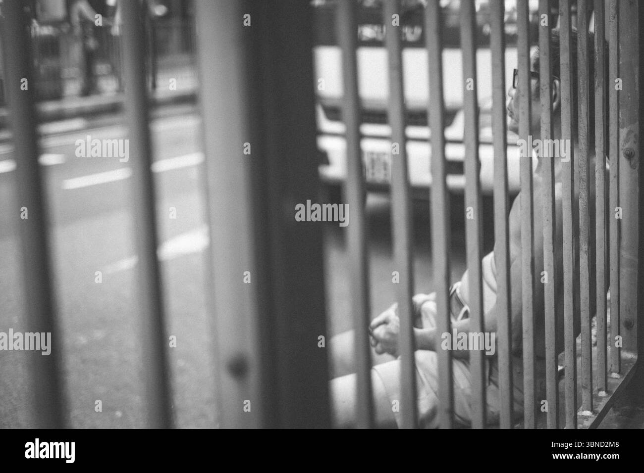 Un homme s'appuie contre une clôture dans les rues animées de Hong Kong, capturé dans un moment de réflexion tranquille au milieu de l'agitation urbaine. Banque D'Images
