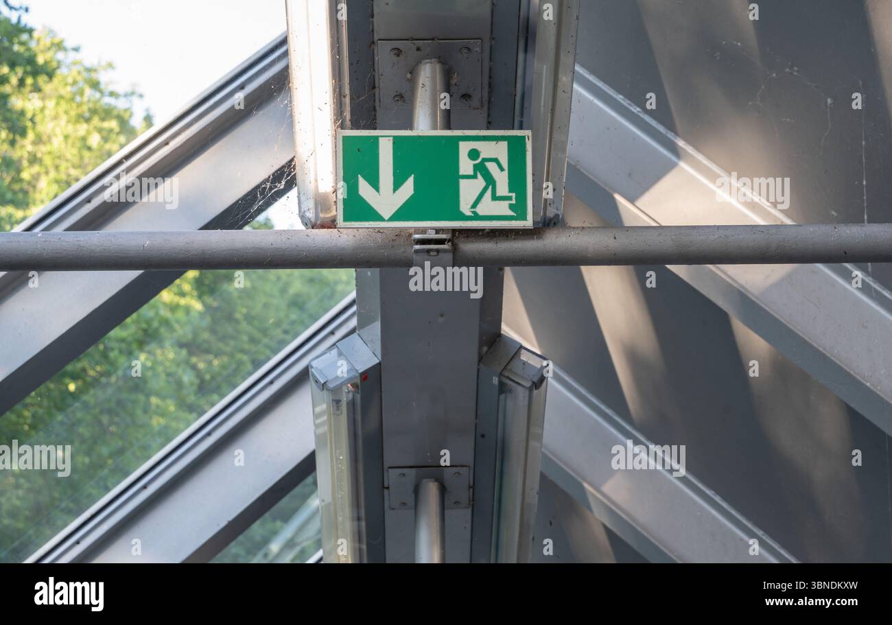 Un panneau de sortie de secours indiquant une voie d'évacuation descendante, qui est bien en vue dans un bâtiment en verre moderne Banque D'Images