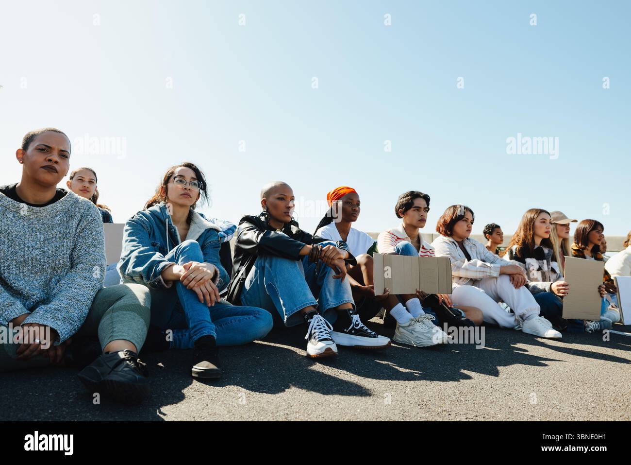 Un groupe de jeunes adultes divers sont assis sur le sol, exprimant leur solidarité lors d'une manifestation en plein air. Ils font preuve d'un sens de la communauté et s'y tiennent Banque D'Images