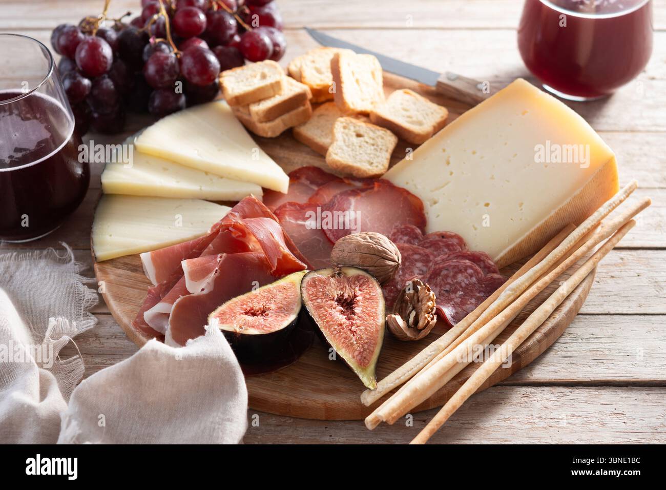 Une planche de charcuterie rustique en bois avec assortiment de fromages, charcuteries, figues fraîches, noix, raisins rouges, et des gressins Banque D'Images