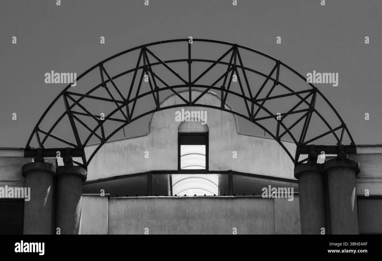 Arche métallique construction encadrant fenêtre ensoleillée au sommet du bâtiment contre le ciel. Teintes monochromes. Banque D'Images