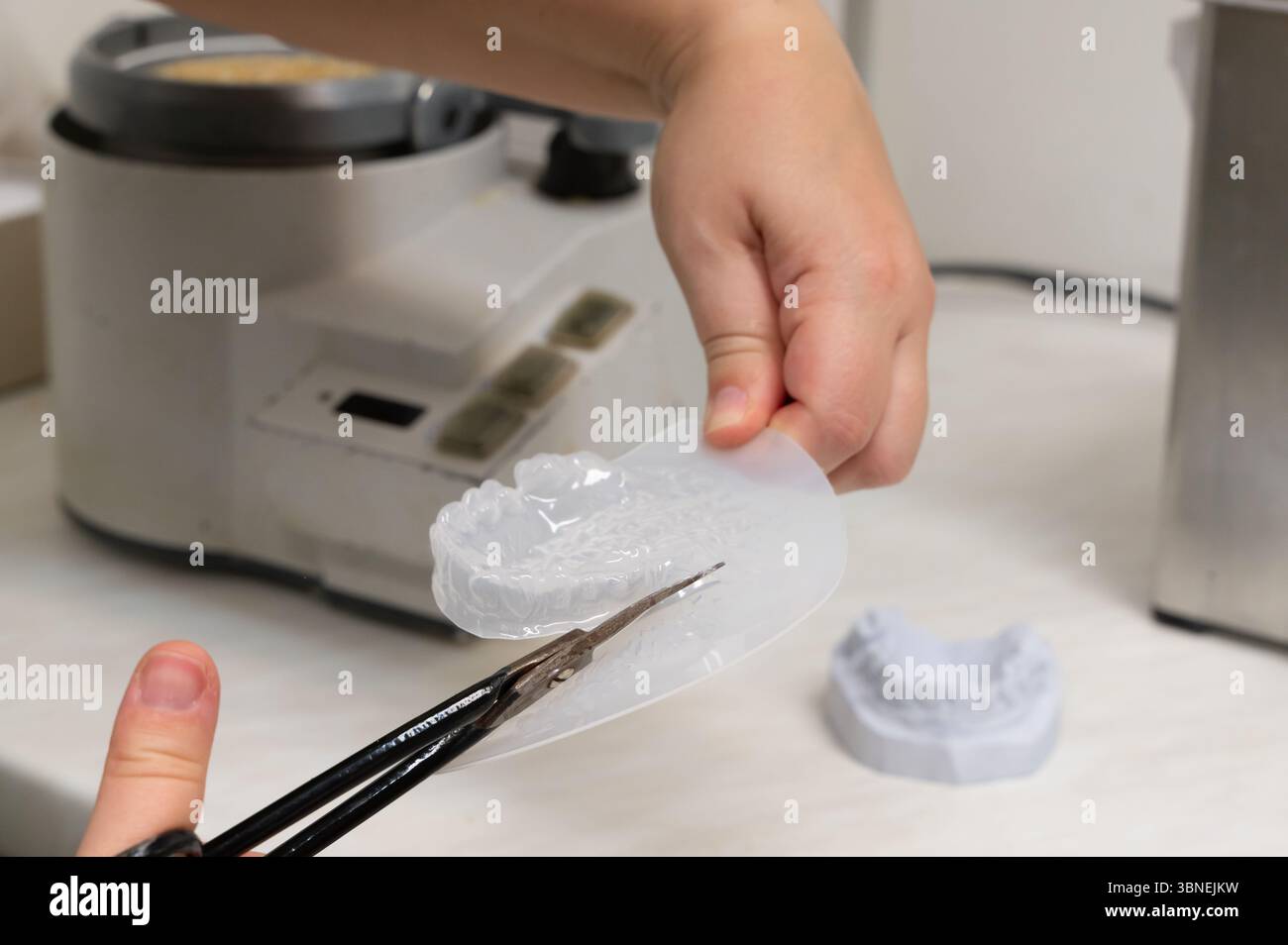 Une main utilisant habilement des ciseaux pour couper avec précision un matériau de moule dentaire dans un cadre de laboratoire dentaire Banque D'Images