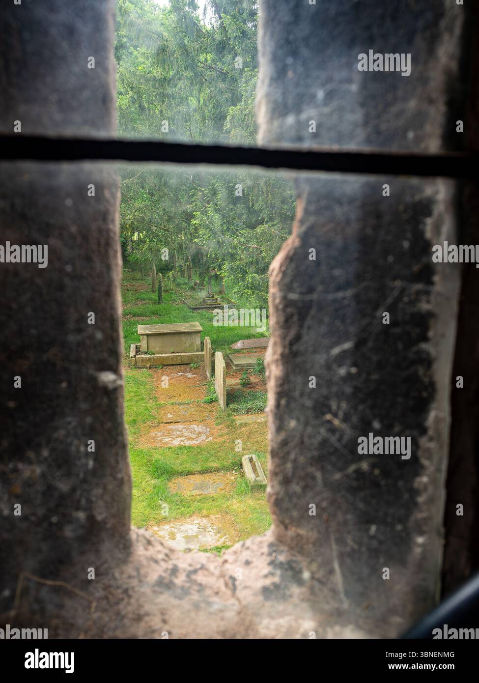 Vue de la cour de la tombe de l'église depuis une fenêtre fendue dans la tour de St.James la Grande église à Gawsworth, Cheshire. Banque D'Images