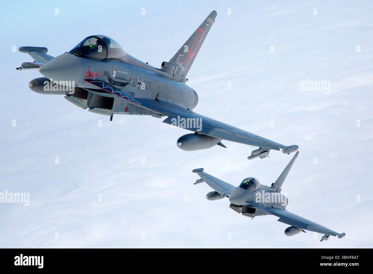 Deux avions Luftwaffe Eurofighter EF‑2000 Typhoon S, y compris le vol. 30+90 (série GS069) et 30+33 (série GS021), volent en formation au large de Wittmundhafen. Les deux sports centenaires de peintures commémoratives célébrant 100 ans de patrimoine unitaire. Les chasseurs canard-delta bimoteurs font preuve d'un positionnement en vol coordonné et d'une conception multirôle moderne. Banque D'Images