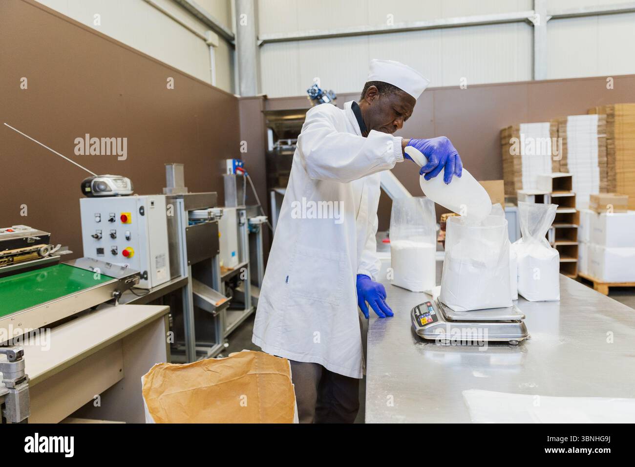 Travailleur ajoutant du glucose à un sac en plastique sur balance pendant le processus d'emballage. Banque D'Images