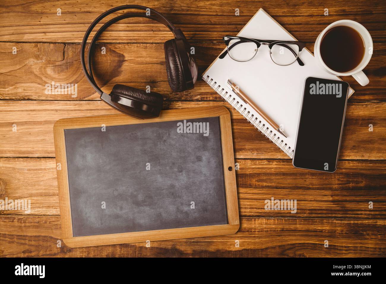 Tablette blanche de style tableau noir repose sur un bureau en bois, montrant casque, smartphone, café Banque D'Images