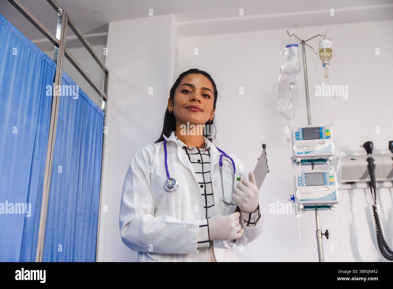 Une femme médecin confiante se tient dans un cadre hospitalier, tenant une planche à pince et portant un manteau blanc et un stéthoscope, signifiant professionnalisme et h. Banque D'Images
