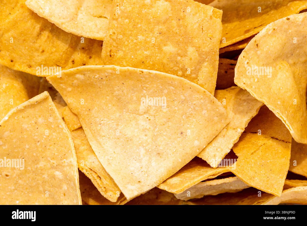 Une image en gros plan mettant en valeur la texture des chips de tortilla croustillantes, soulignant leur couleur dorée naturelle et leur surface rugueuse. Idéal pour une utilisation comme backgr Banque D'Images
