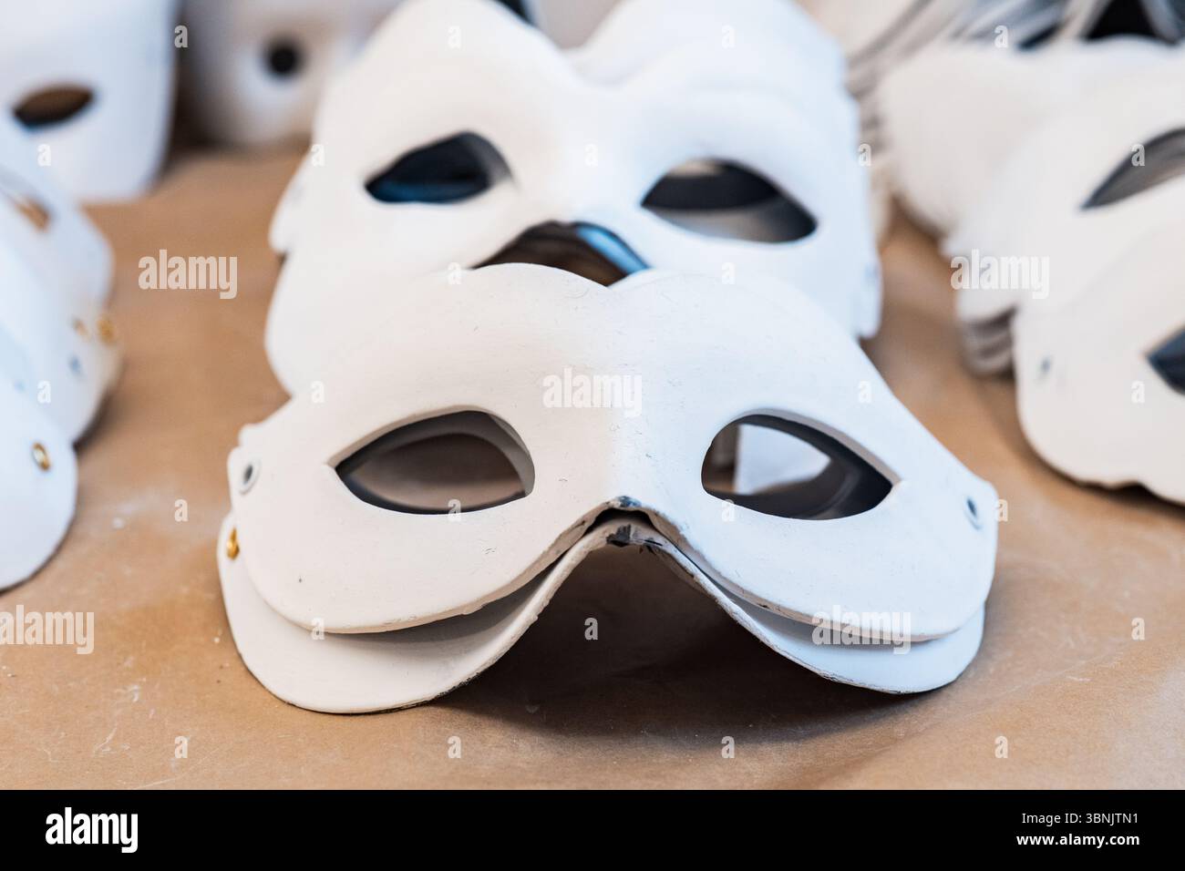 Des masques blancs sont exposés dans un atelier de Venise, mettant en valeur l'artisanat traditionnel. Les dessins détaillés reflètent le riche patrimoine culturel et artistique de la ville Banque D'Images