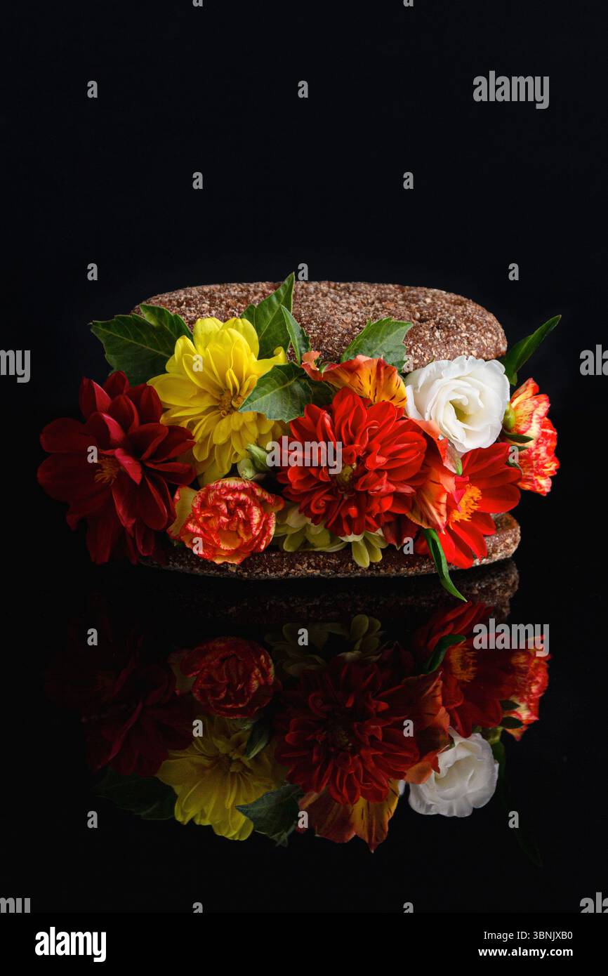 Un sandwich unique habilement arrangé avec des fleurs rouges, jaunes et blanches vives entre deux tranches de pain noir. Les fleurs créent un contraste époustouflant Banque D'Images