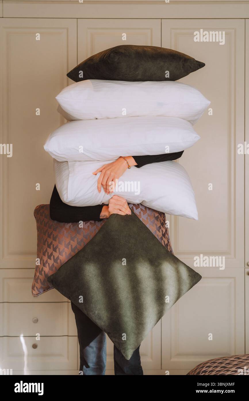 Une personne se tient cachée derrière une pile d'oreillers moelleux dans une chambre d'hôtel confortable. Les coussins doux et invitants créent un sentiment de luxe et de confort, parfait Banque D'Images