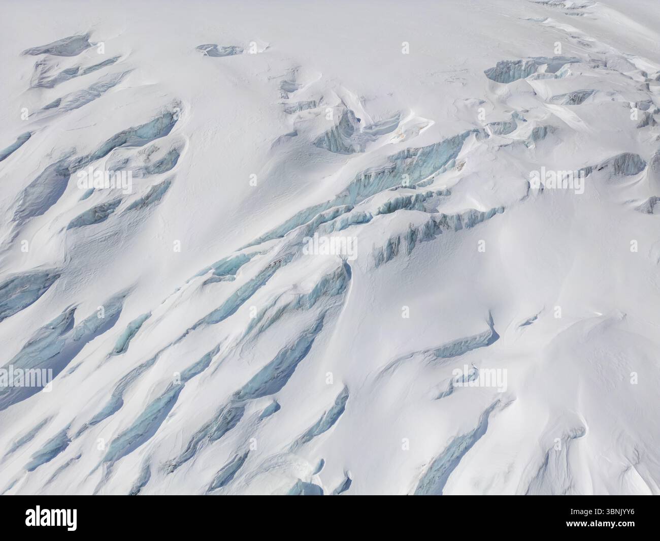Une vue aérienne à couper le souffle d'un glacier dans les Alpes suisses, mettant en valeur de vastes champs de glace et de neige avec des crevasses profondes, soulignant la beauté et fra Banque D'Images