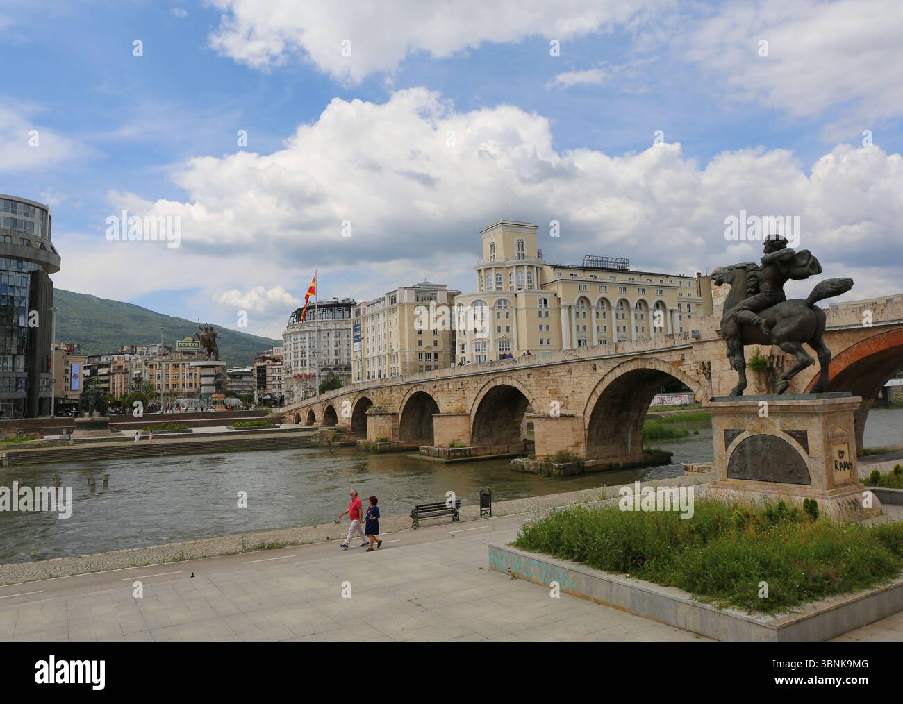 Skopje, Macédoine du Nord-28 mai 2025 : couple non identifié marchant près de la rivière Vardar et Pont de pierre de l'ère ottomane Banque D'Images