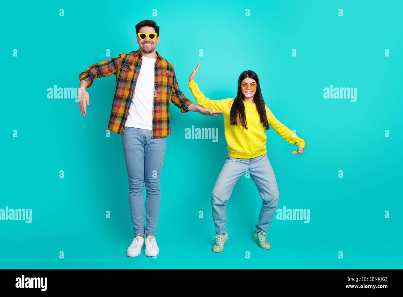 Jeune couple énergique dans des tenues décontractées vibrantes posant de manière ludique sur un fond turquoise lumineux, mettant en valeur la joie Banque D'Images