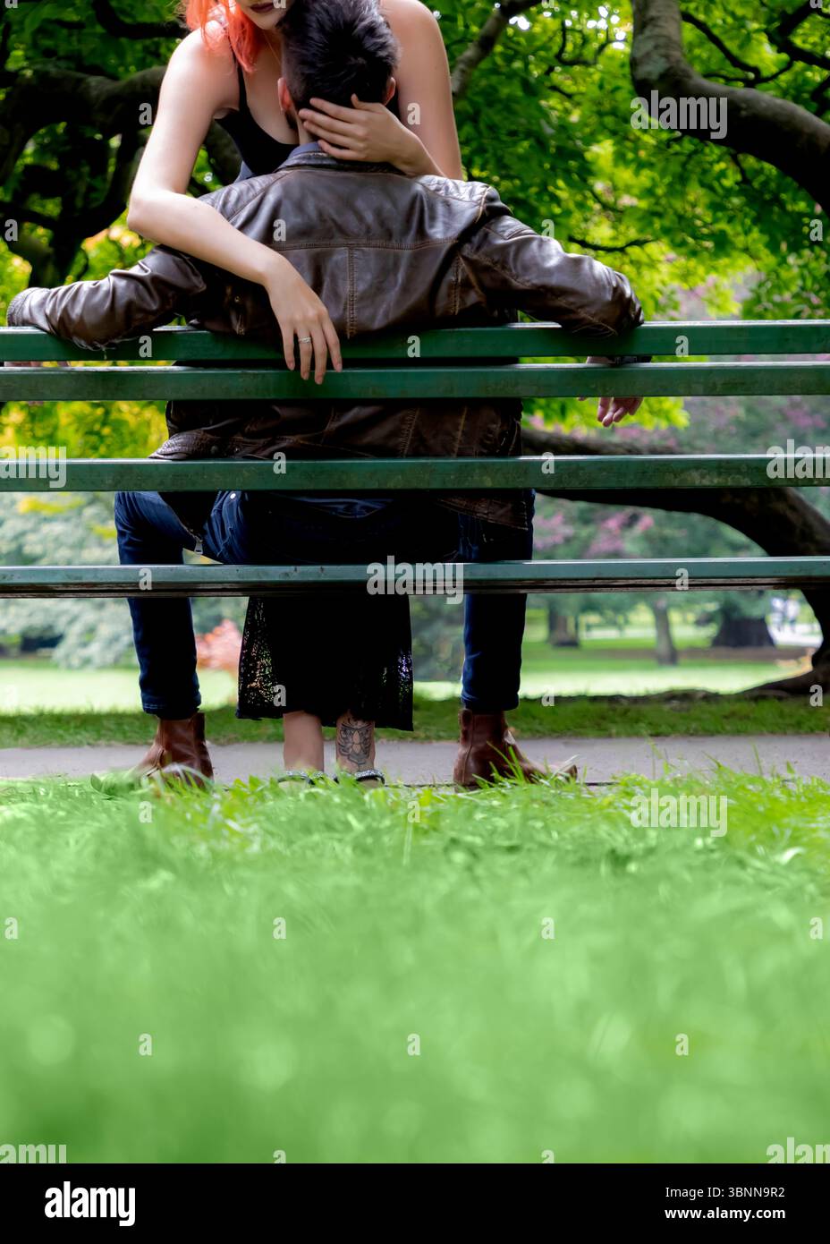 Un couple s'embrasse sur un banc de parc. La femme aux cheveux roux tient la tête de l'homme, alors qu'il est appuyé en arrière contre le banc. La scène est réglée Banque D'Images