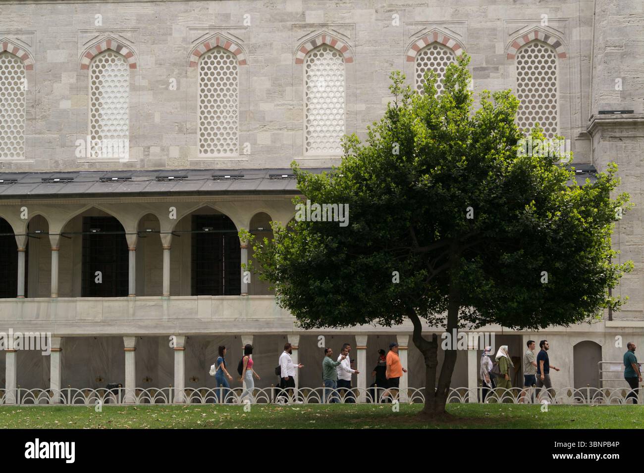 Les gens marchent tranquillement à travers une belle cour à Istanbul, entourée de verdure luxuriante et de structures historiques par une journée agréable. Banque D'Images