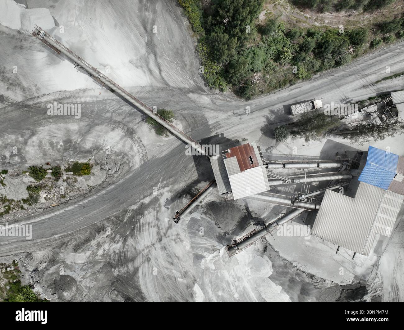 Vue aérienne par drone de l'usine de concassage de pierre industrielle avec des bandes transporteuses et camion à l'usine de traitement de calcaire entourée de forêt, montrant Banque D'Images