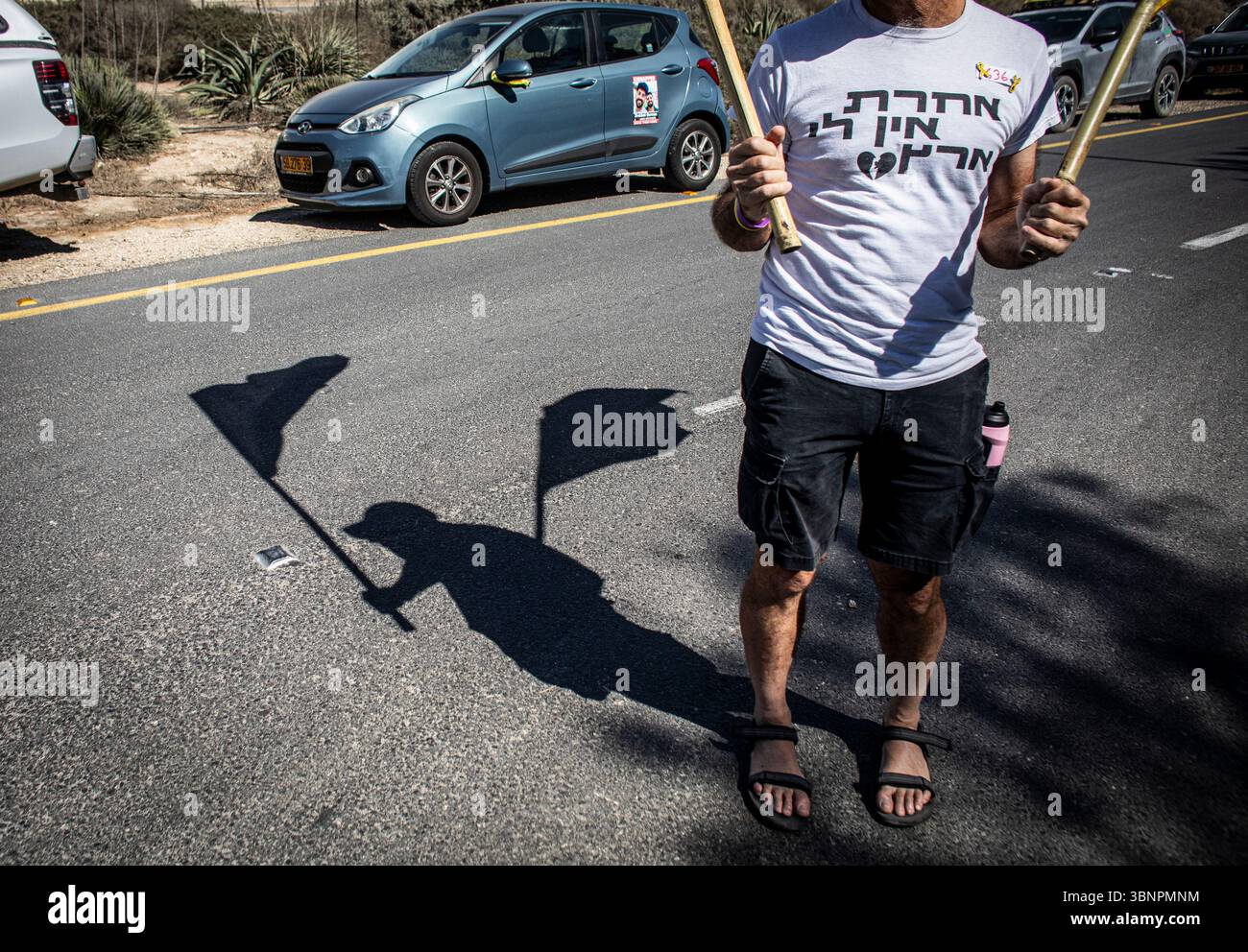 Un manifestant porte deux drapeaux à l’entrée du kibboutz Nir Oz avant la visite du premier ministre israélien Benjamin Netanyahu, jeudi 3 juillet 2025. Netanyahu a effectué sa première visite depuis le massacre du 7 octobre dans la communauté frontalière de Gaza du kibboutz Nir OzÑnearly 21 mois après l’assaut mené par le Hamas qui a laissé un résident sur quatre assassiné ou kidnappedÑand a été accueilli à l’entrée par une pancarte indiquant ÒMr. AbandonmentÓ et par des survivants en colère l'accusant de chercher la rédemption politique sans jamais reconnaître l'échec de stateÕs à les protéger. Photo par Eyal Warshavsky. Banque D'Images